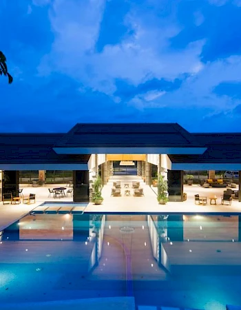 A luxurious resort with a large, illuminated swimming pool at dusk, featuring modern architecture and a serene ambiance.