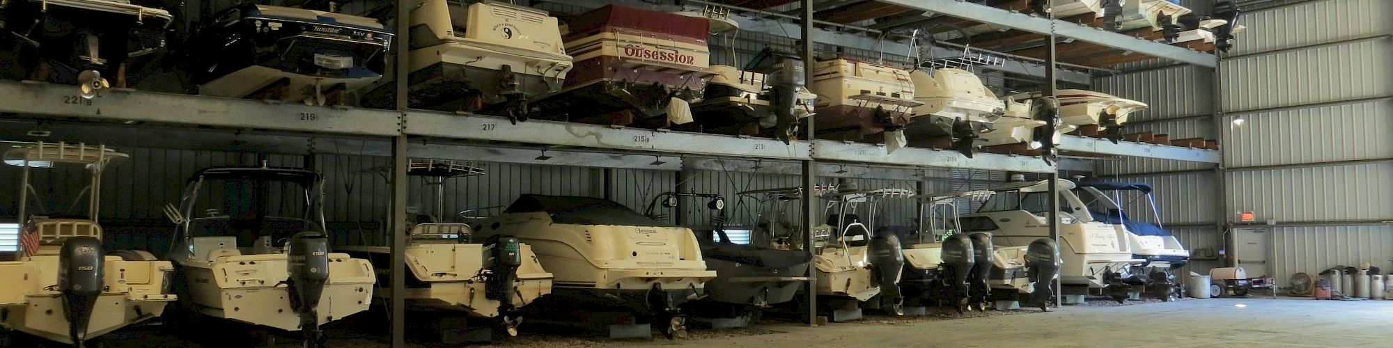 The image shows a large indoor storage facility with multiple rows of boats stacked on racks, creating an organized, multi-level arrangement.