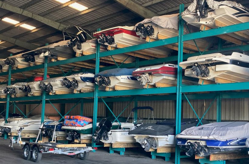 The image shows a warehouse storing multiple boats stacked on racks. Several rows and columns of boats are neatly organized and covered.