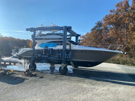 The image shows a large boat being transported on a hydraulic boat lift at a marina, surrounded by autumn trees and clear blue sky.