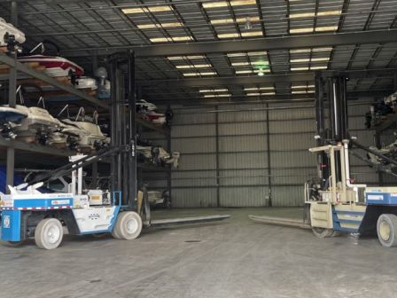 The image shows a storage facility with boats stacked on racks and two forklifts parked inside.