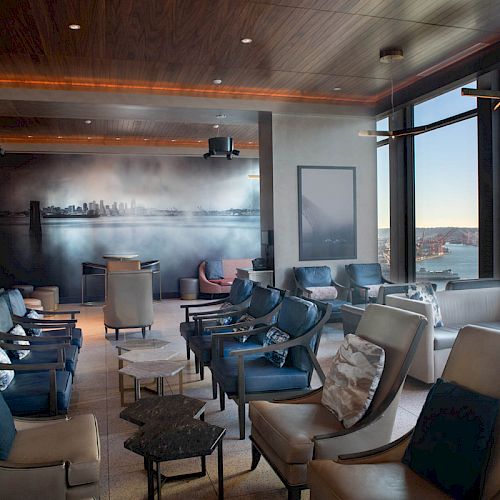 A modern lounge with ample seating, large windows with water views, a wall mural, and a cozy, inviting atmosphere.